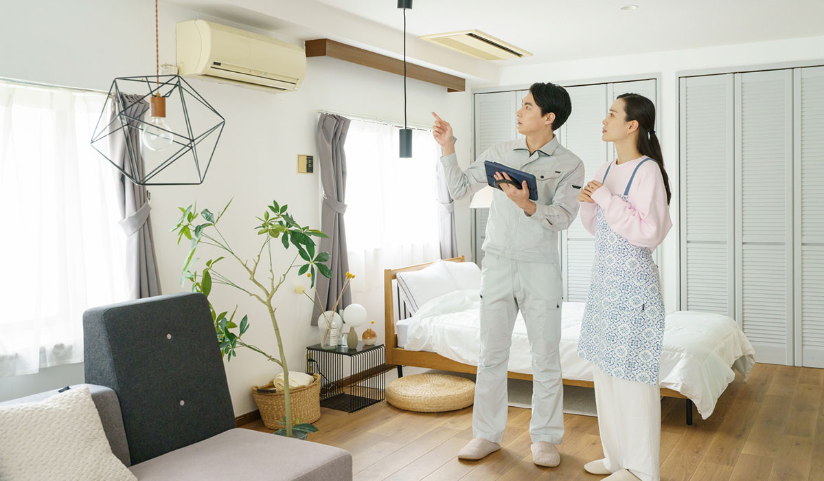 室内でエアコンを指し示しながら状態を確認している作業員と女性のイメージ